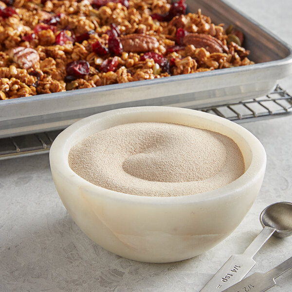 A bowl of granola with pecans and a measuring spoon filled with Nielsen-Massey Madagascar Bourbon Pure Vanilla Powder.