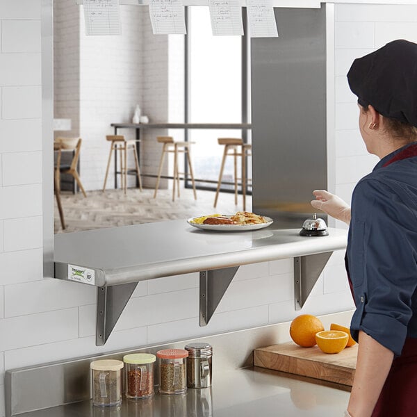 A woman in a kitchen with a Regency stainless steel shelf on the wall above the counter.