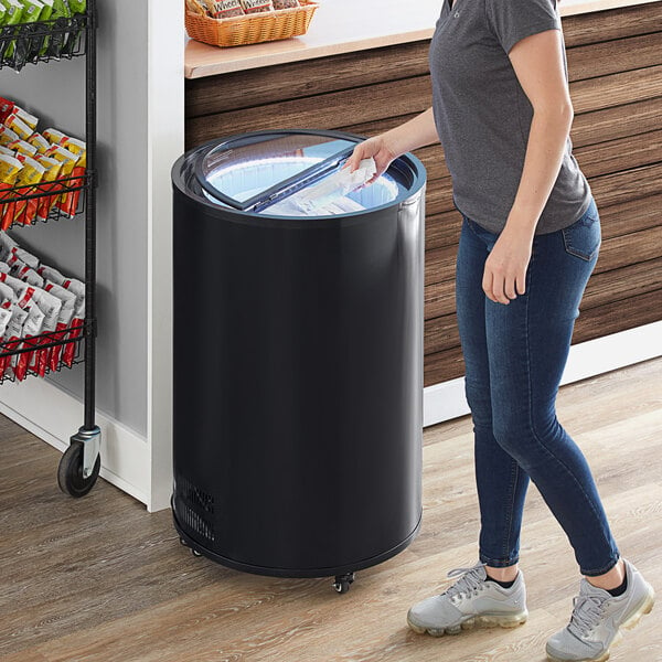 A woman standing next to a black Galaxy BMF3-B merchandiser freezer with a white top.