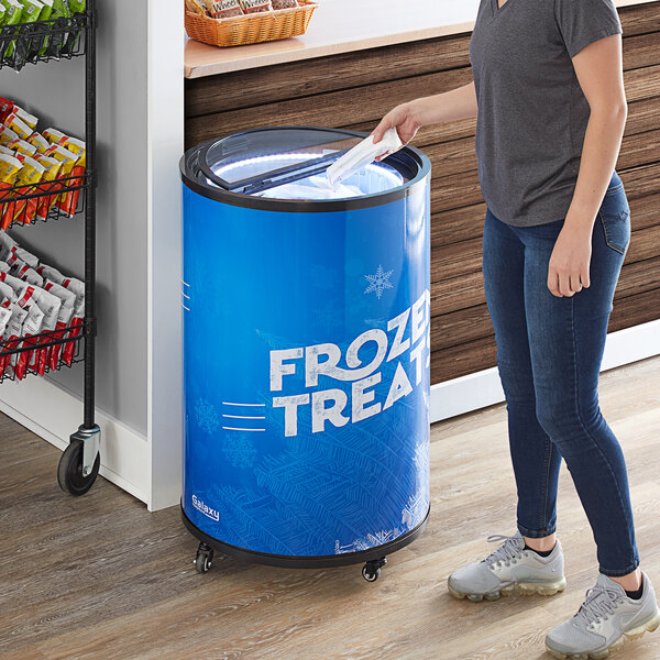 A woman standing next to a blue Galaxy Glass Door Merchandiser Freezer.
