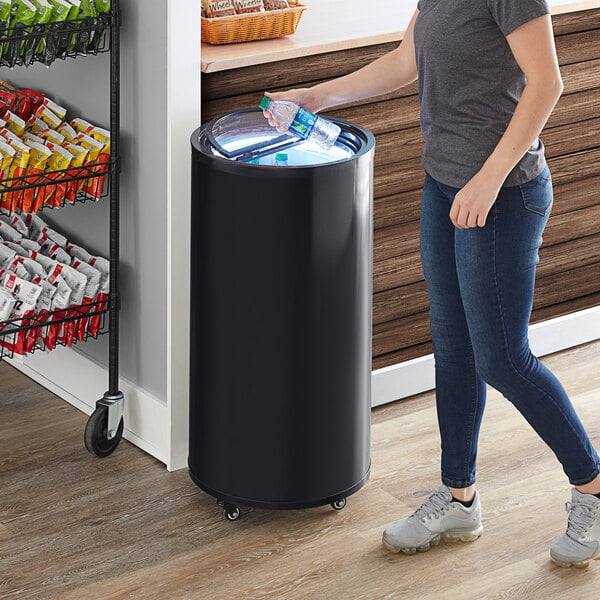 A woman standing next to a Galaxy barrel merchandiser refrigerator with a plastic bottle.