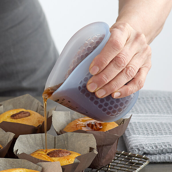 A hand using an OXO Good Grips silicone measuring cup to pour syrup over muffins.