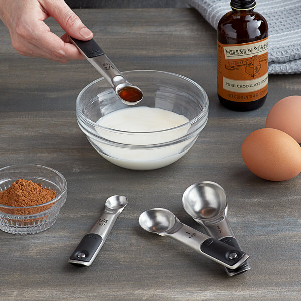 A person using an OXO stainless steel measuring spoon over a bowl of brown powder.