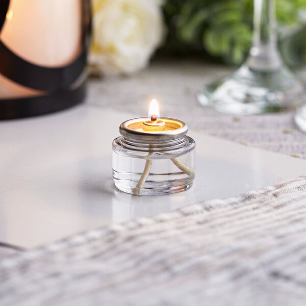 A Leola liquid paraffin candle burning in a glass container on a table.