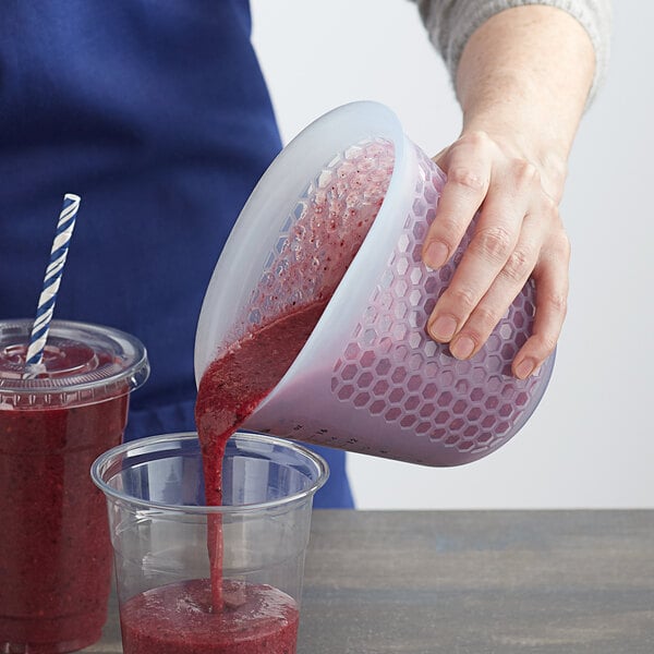 A person using an OXO Good Grips Squeeze & Pour measuring cup to pour a smoothie into a plastic cup.