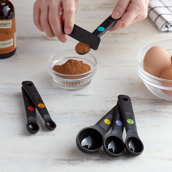 A person using black OXO measuring spoons to add brown powder to eggs.