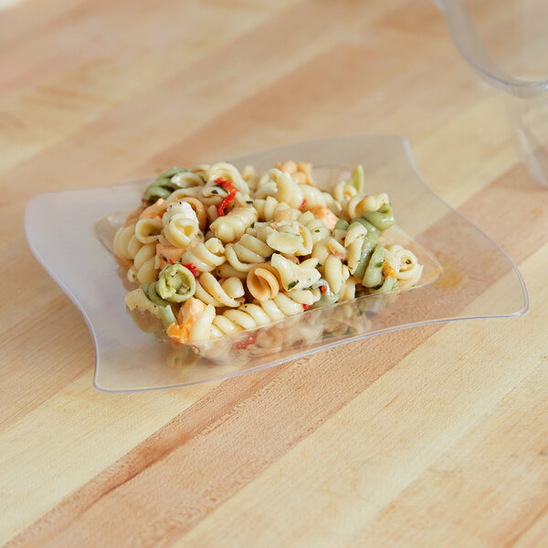 A clear plastic bowl filled with pasta on a wood surface.