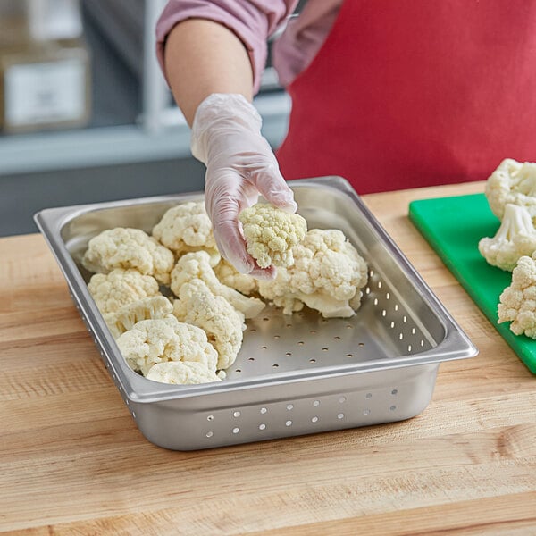 A person wearing gloves holding cauliflower in a Choice stainless steel pan.