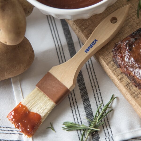 A Carlisle Sparta Boar Bristle Pastry Brush with sauce on a cutting board.