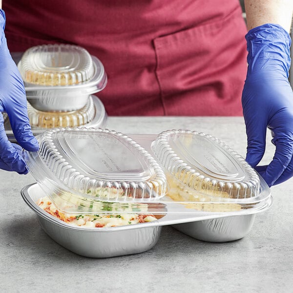A person in blue gloves holding a ChoiceHD silver foil container with food.