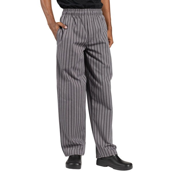 A person wearing Uncommon Chef gray and black striped chef pants with their hands in their pockets.