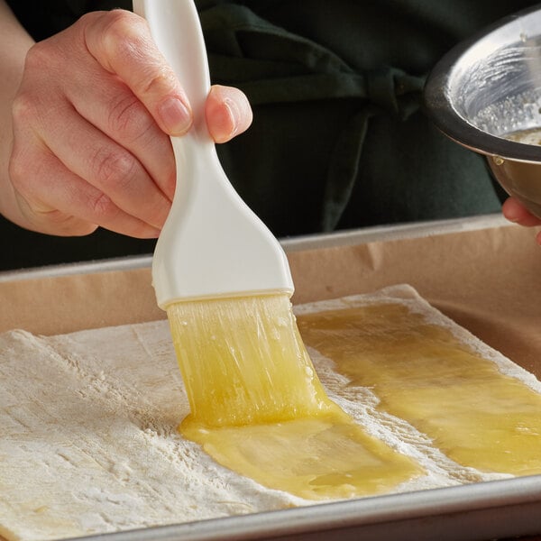 A hand using a white Carlisle Sparta Spectrum pastry brush to spread butter on a piece of bread.