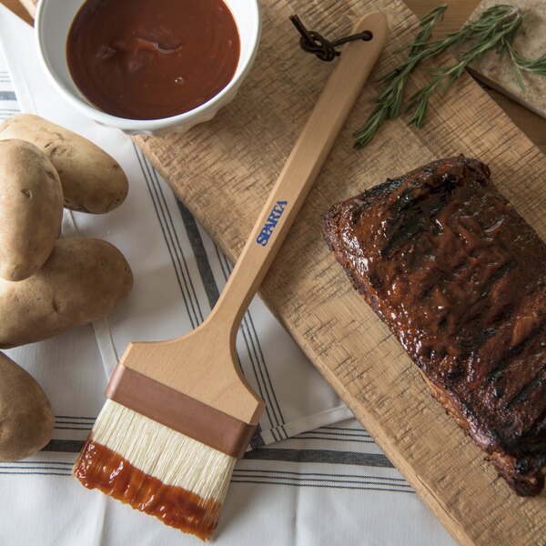 A Carlisle Sparta Chef Series basting brush on a cutting board with meat and potatoes.
