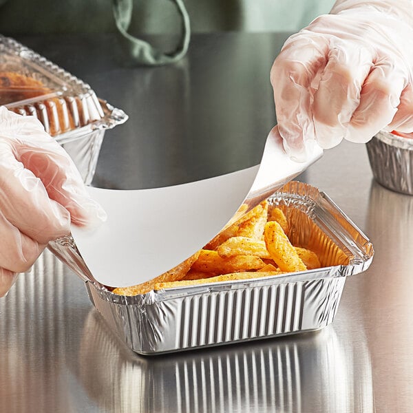 A person in a plastic glove putting a paper in a Choice oblong foil container over a tray of french fries.