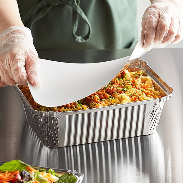 A person in gloves holding a Choice oblong foil container with food over a paper tray.