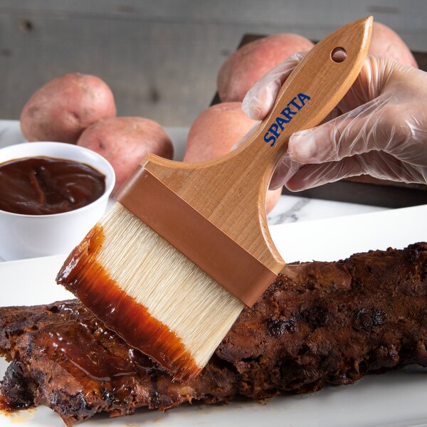 A person painting meat with a Carlisle boar bristle pastry brush.