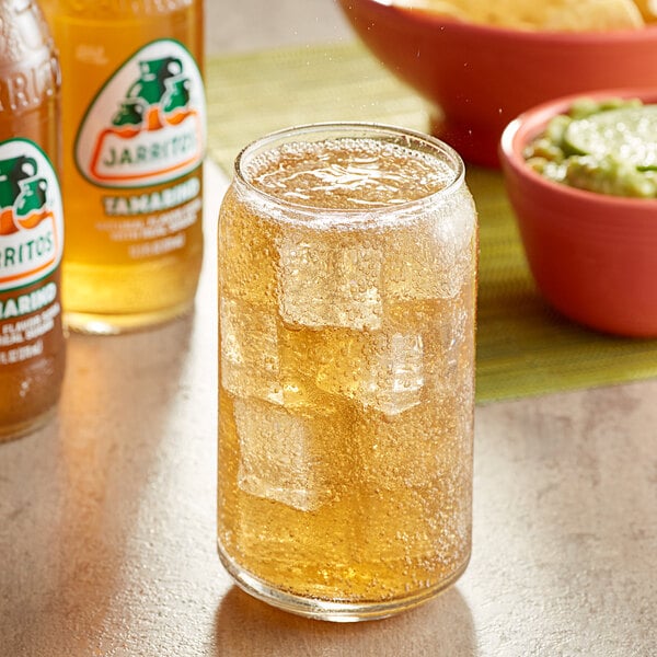 A glass of Jarritos Tamarind soda with ice and a bowl of chips.