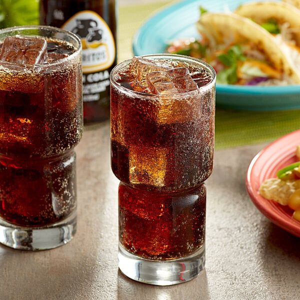 A glass of Jarritos Mexican Cola with ice and a taco on a plate.