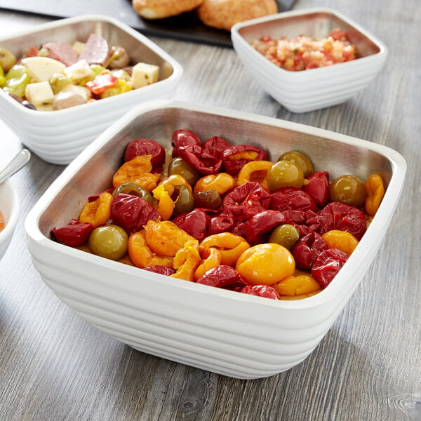 A Vollrath Pearl White metal serving bowl filled with food on a table.