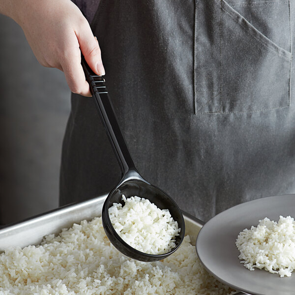 A person holding a Carlisle black long handle portion spoon over a bowl of rice.