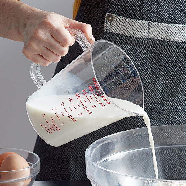 A person pouring milk from a plastic bag into a Carlisle clear polycarbonate measuring cup.