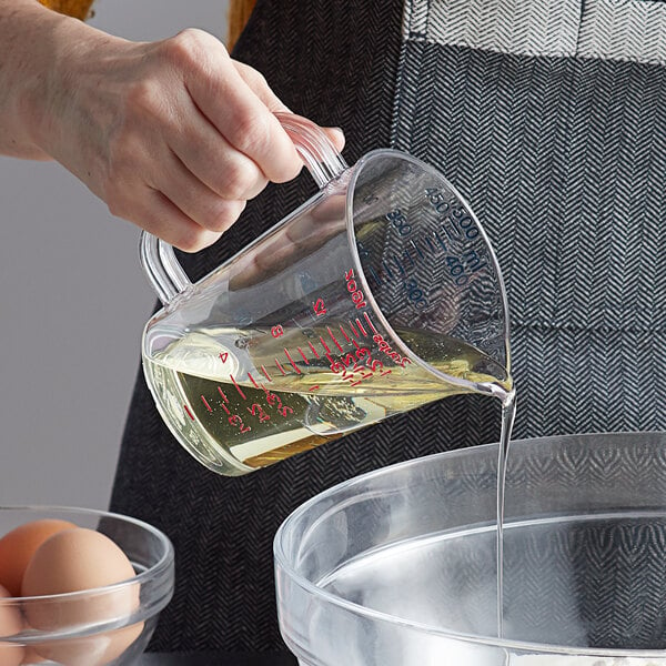 A hand holding a Carlisle clear polycarbonate measuring cup pouring liquid into a bowl of eggs.