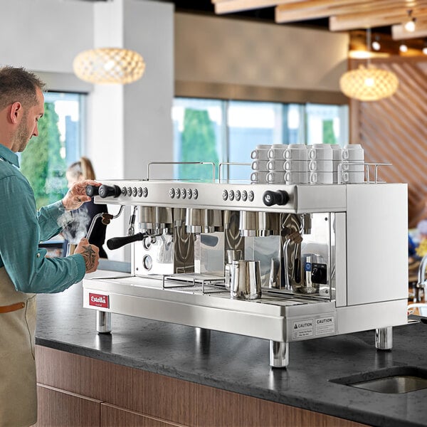A man standing at a counter with an Estella Caffe three group automatic espresso machine.