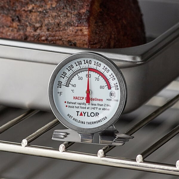 A Taylor 5980N professional hot holding thermometer on a pan of meat.