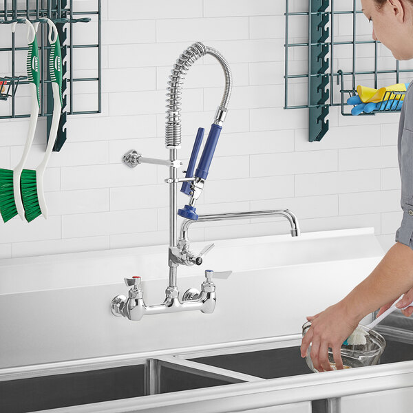 A woman using a Waterloo wall-mounted pre-rinse faucet to wash dishes in a kitchen sink.