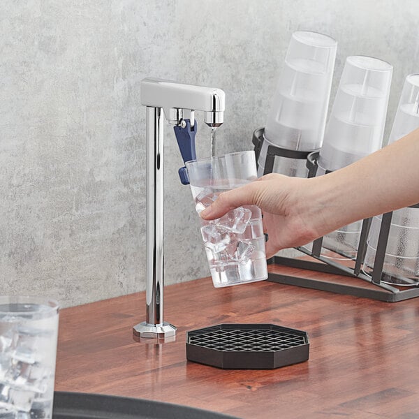 A hand using a Waterloo countertop glass filler to pour water over ice in a glass.