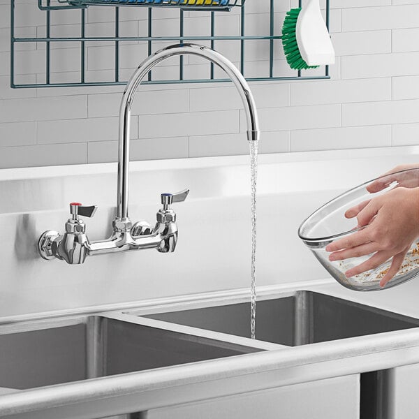 A person washing a bowl in a sink with a Waterloo wall mount faucet.
