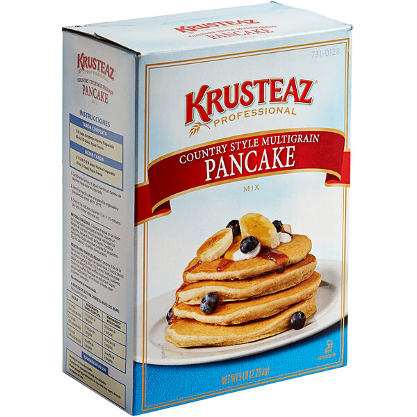 A box of Krusteaz country-style multigrain pancake mix with a stack of pancakes topped with berries and bananas.