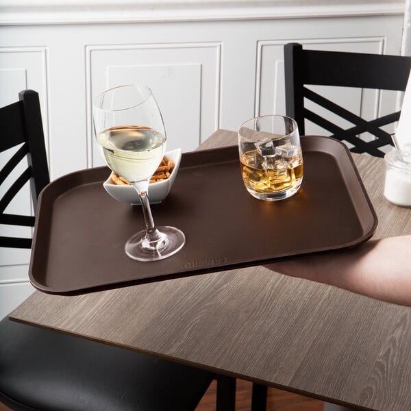 A hand holding a Cambro Tavern Tan non-skid tray with two glasses of wine and a bowl of ice cubes.