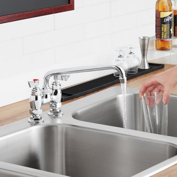 A woman pouring water from a Waterloo 10" swing spout into a glass over a stainless steel sink.