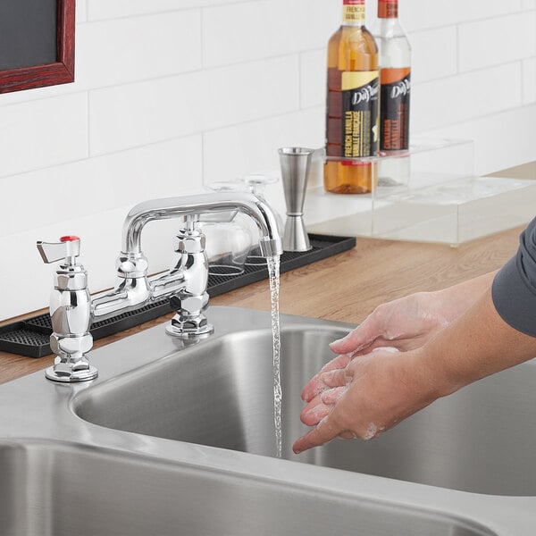 A person washing their hands under a Waterloo swing spout in a professional kitchen.