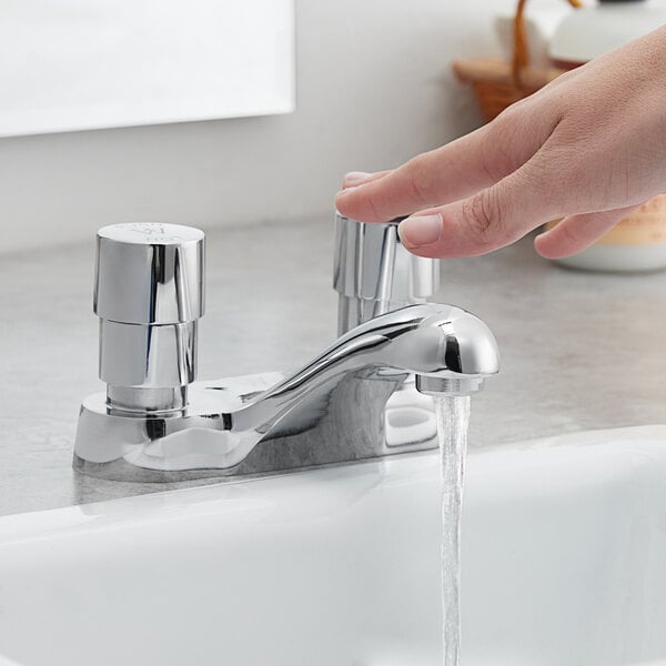 A hand pressing a Waterloo deck-mounted metering faucet over a sink.