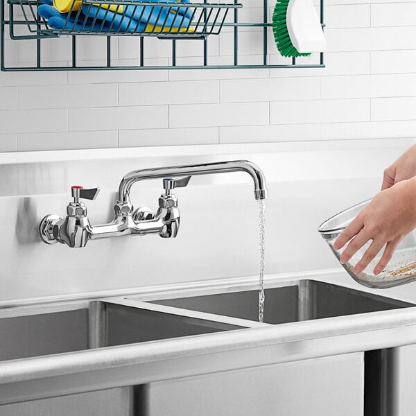 A hand washing a bowl of water using a Waterloo wall-mounted faucet.