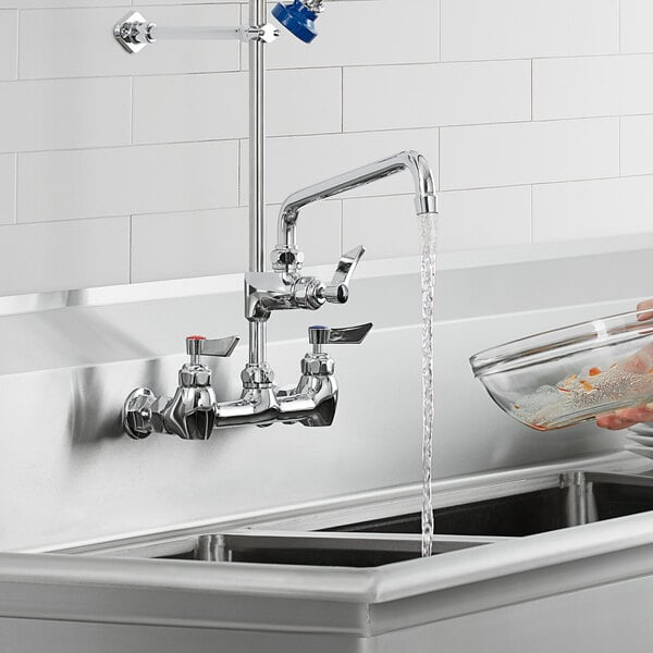 A person using a Waterloo pre-rinse add-on faucet to wash a glass bowl in a kitchen sink.