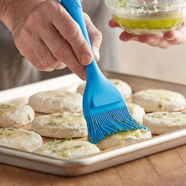 A person using an Ateco flat silicone bristle pastry brush to brush food.