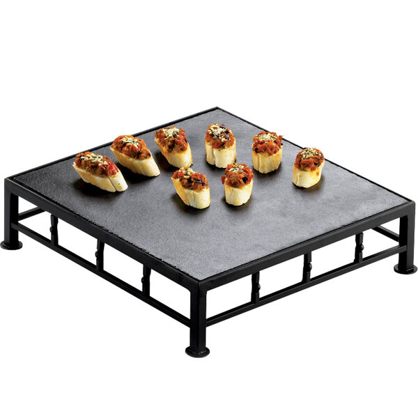 A Cal-Mil black metal square riser with food on a slate top tray.