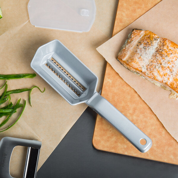 A Westmark aluminum fish scaler on a cutting board next to a piece of fish.