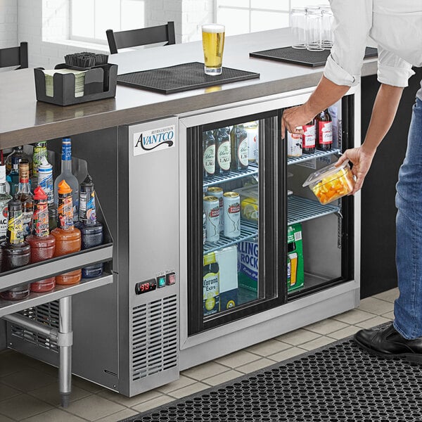 A man opening a Avantco back bar refrigerator with drinks.