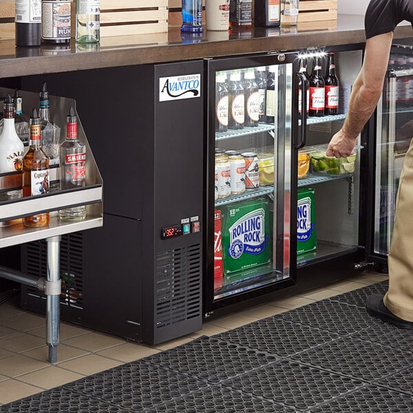 A man standing at a bar with an Avantco back bar refrigerator full of drinks.