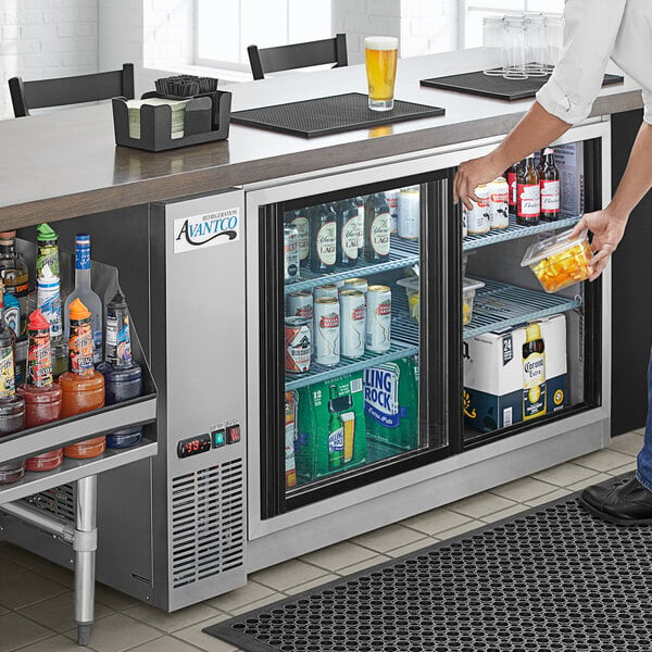 A man putting drinks in a stainless steel Avantco back bar refrigerator with sliding glass doors.