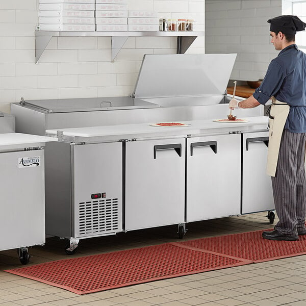 A chef preparing food in a commercial kitchen at an Avantco 3 door refrigerated pizza prep table.