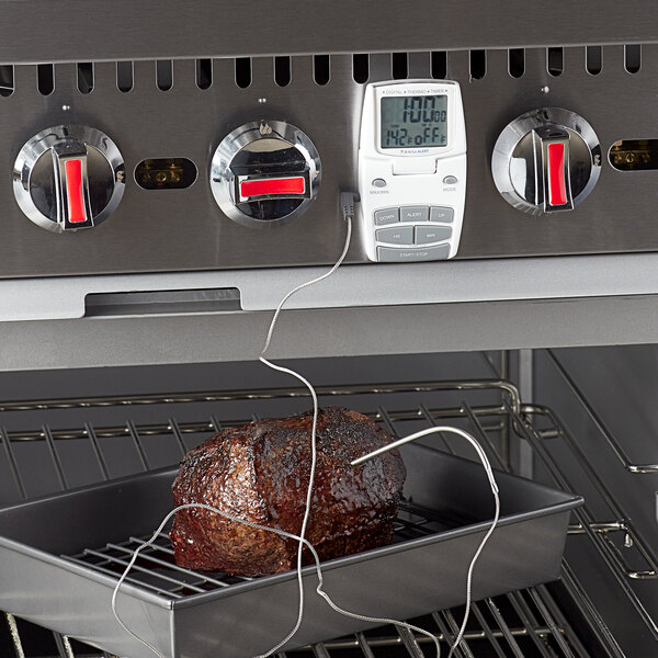 A Comark digital cooking thermometer with a piece of meat on a tray in an oven.