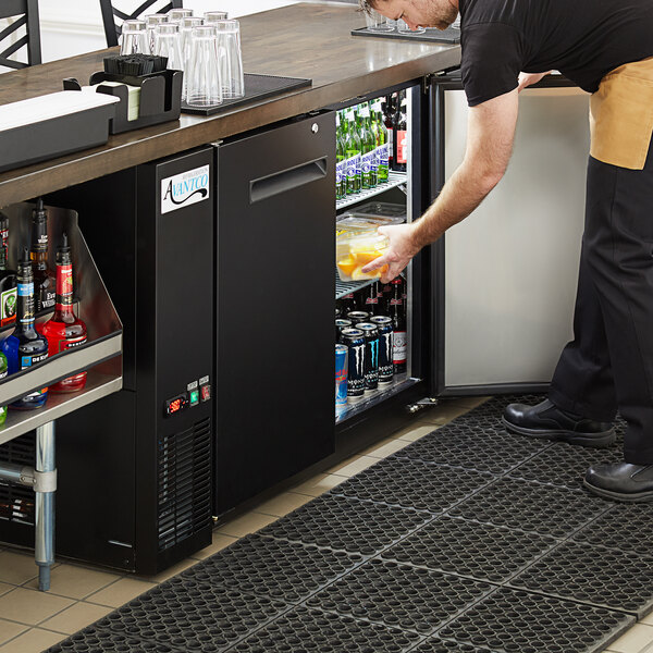 A man putting a beverage into a black Avantco back bar refrigerator.