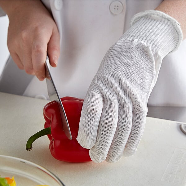 A person wearing a MercerGuard white cut-resistant glove cutting a red pepper.