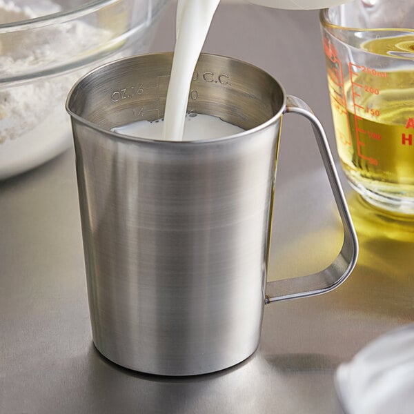 A person pouring milk into a Vollrath stainless steel measuring cup.