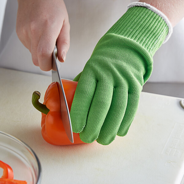 A person wearing green Mercer Culinary cut-resistant gloves cutting a pepper with a knife.